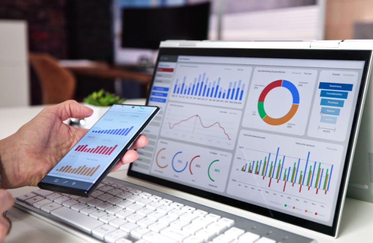 Person Using Phone and Laptop to Look at KPIs and Data