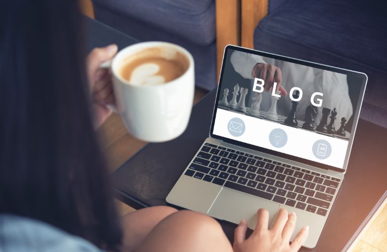 Woman Holding Coffee and Looking at a Blog on a Laptop