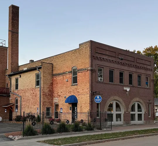 Two-story brick building with arched windows, blue awning, and a surrounding black iron fence.