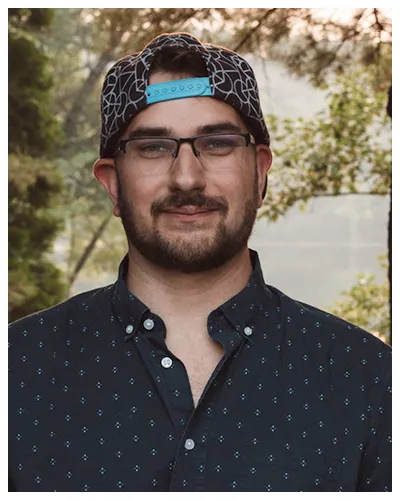 Portrait of a man wearing glasses and a patterned baseball cap outdoors.