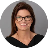Professional headshot of a smiling woman with glasses and brown hair against gray background.