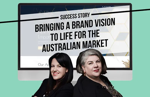 Two professional women standing confidently back-to-back in front of a computer screen displaying text about a brand vision for the Australian market.