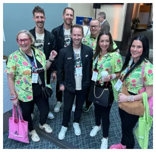 Group of seven adults wearing colorful floral shirts and conference badges, posing indoors.