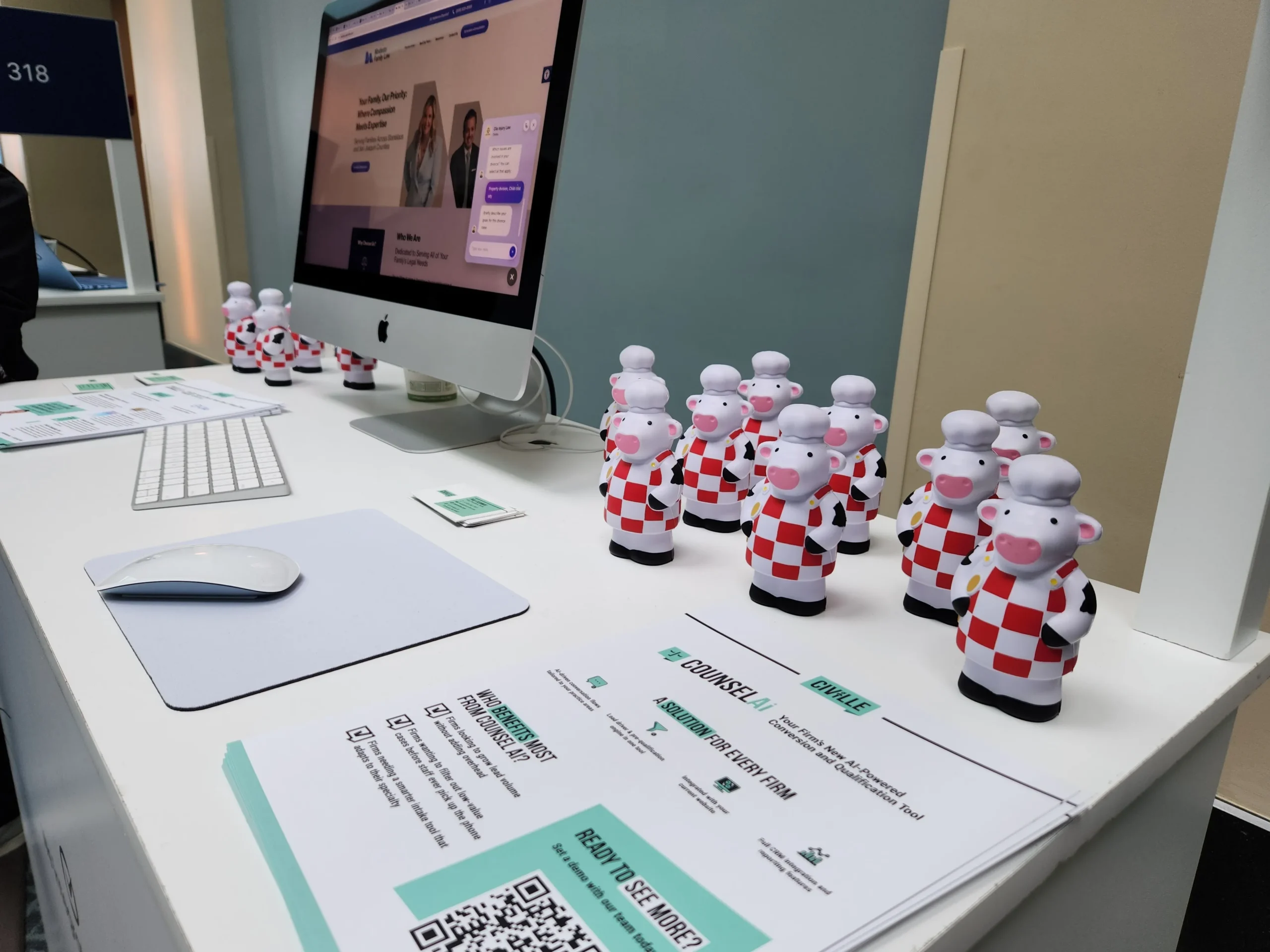 Desktop computer displaying a legal services website, surrounded by cow chef figurines and informational brochures.