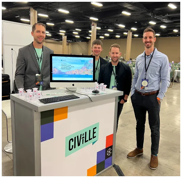 Four men standing behind and beside a Civille-branded booth with a computer monitor displaying a website, in a large indoor event space.