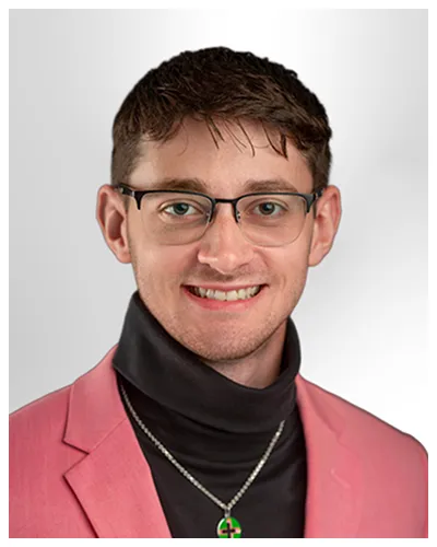 Professional portrait of a young man wearing glasses, a pink blazer, black turtleneck, and a necklace.