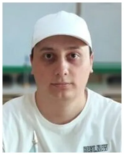 Portrait of a man wearing a white cap and white shirt, neutral background.