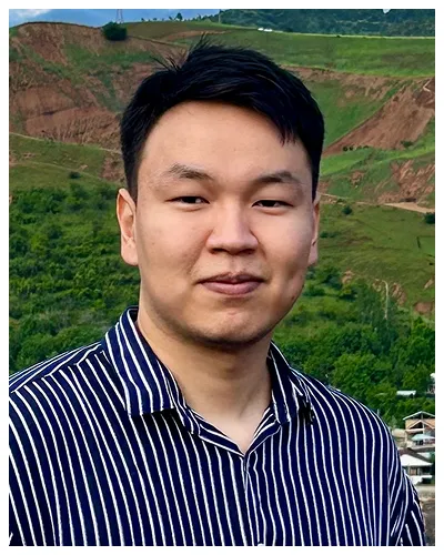 Portrait of a young man with short black hair wearing a black and white striped shirt outdoors.