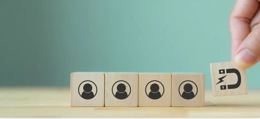 Hand placing wooden block with magnet icon next to four blocks with person icons on wooden surface.