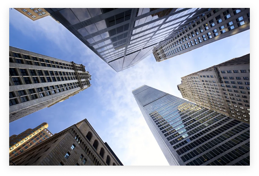 Upward view of tall skyscrapers with glass and stone facades against a blue sky.