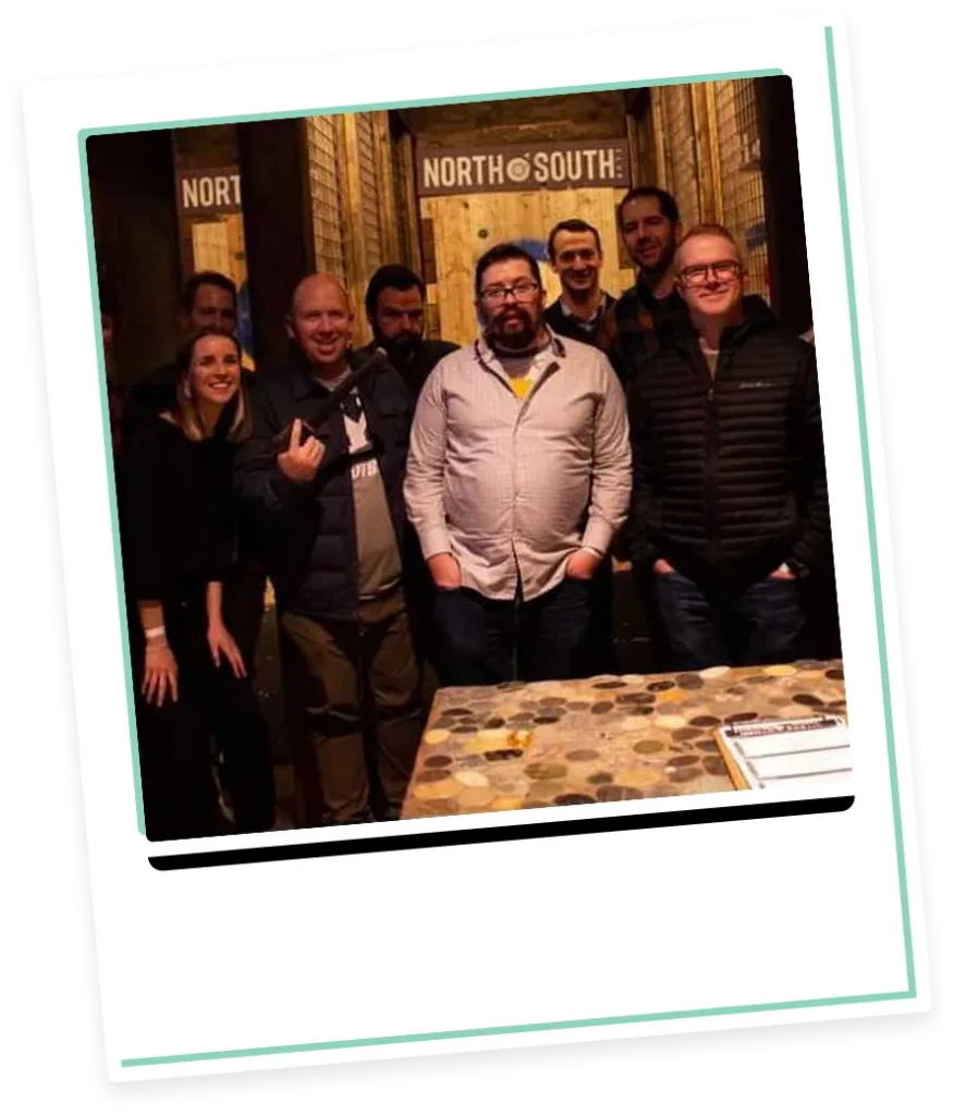 Group of eight adults posing indoors near wooden targets with "NORTH SOUTH" signage.