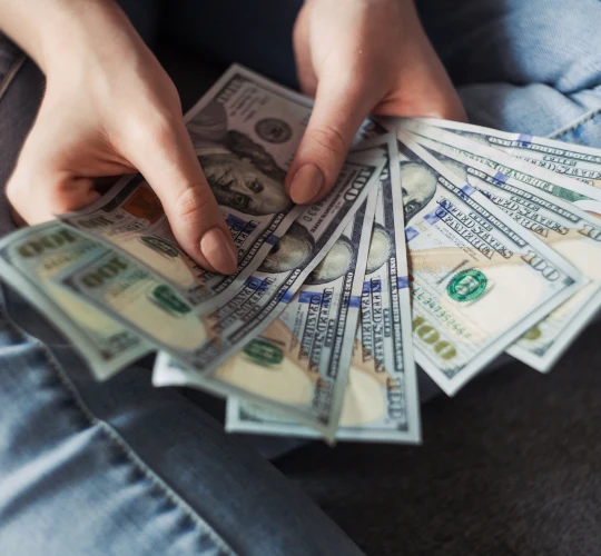 Close-up of hands holding a fan of hundred-dollar bills.