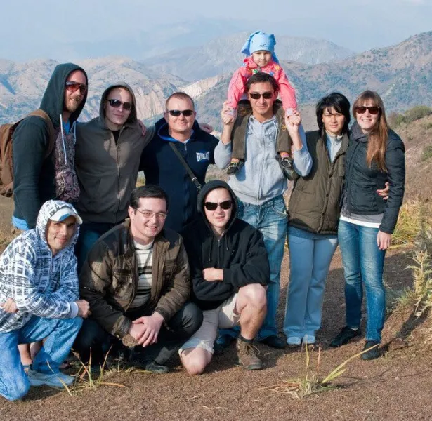 Group of ten people, including one child, posing outdoors with mountainous landscape in the background.