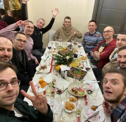 Group of men seated around a festive dining table with food and drinks, smiling and posing.