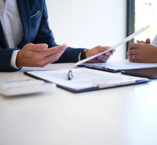 Two professionals in business attire discussing documents at a white table.