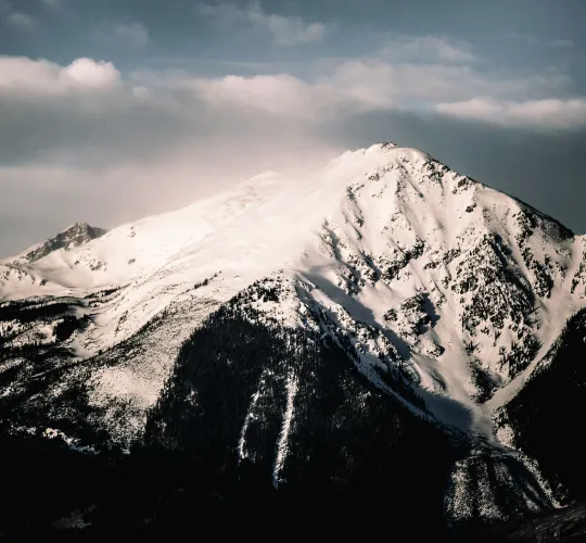 Snow-covered mountain peak under a partly cloudy sky during daytime.