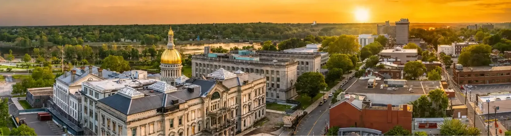 Aerial view of a cityscape at sunset featuring historic buildings and a golden-domed capitol.