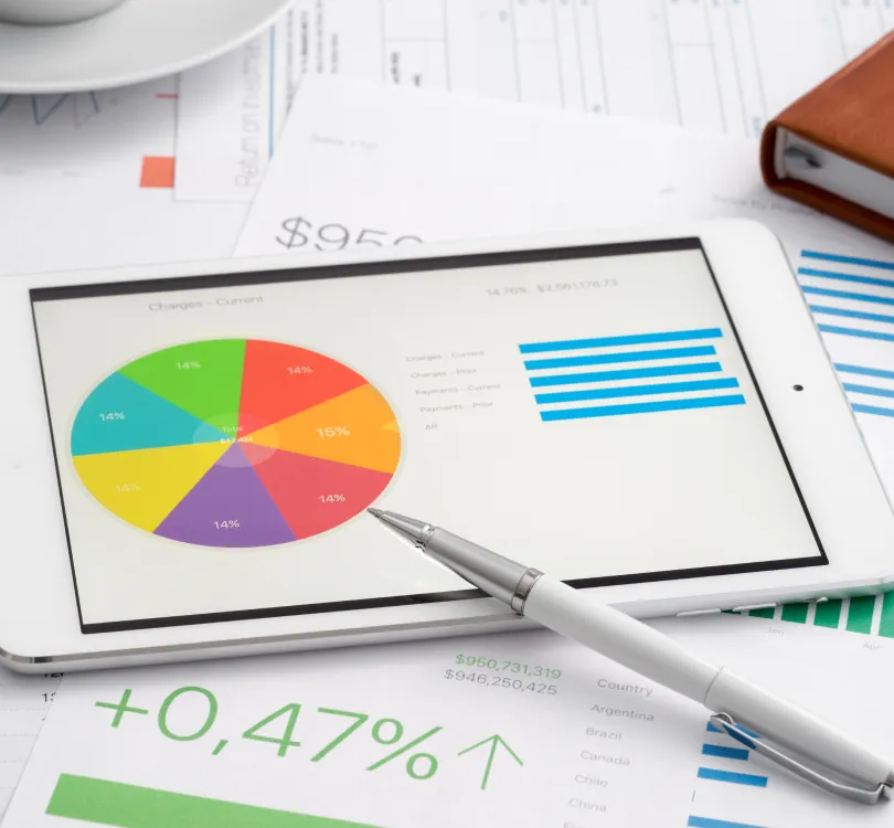 Tablet displaying colorful pie chart and blue bar graph with silver pen on top, surrounded by financial documents.