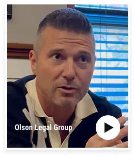 Middle-aged man speaking indoors with blue blinds in background, text "Olson Legal Group.